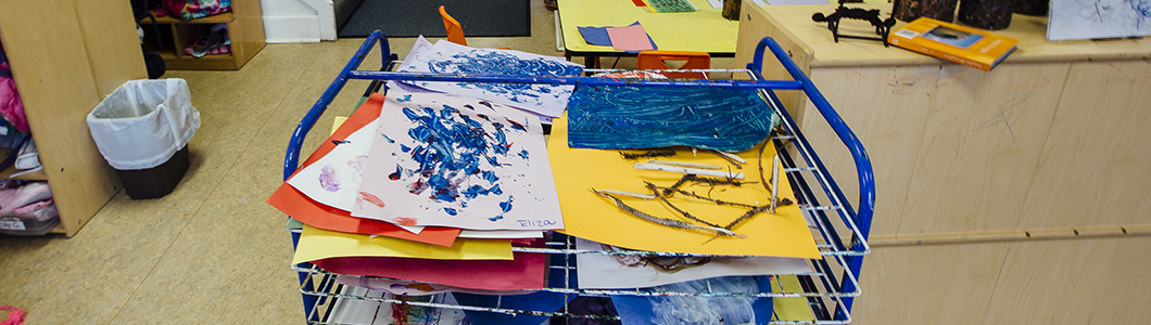 An art drying rack displays piles of children's paintings and drawings.
