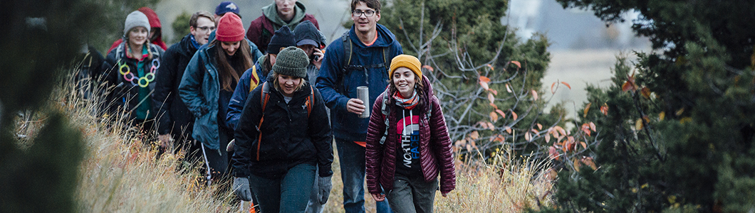 A group of male and female students hike on a trail.