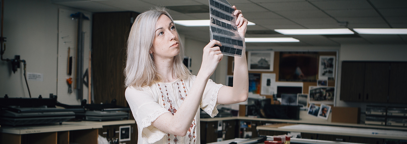 A young woman inspects a sheet of developed film negatives.