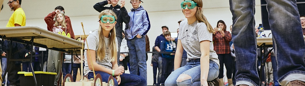 A group of students wearing goggles observe an experiment.