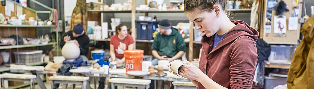 A group of students labor over pottery in a clay studio.