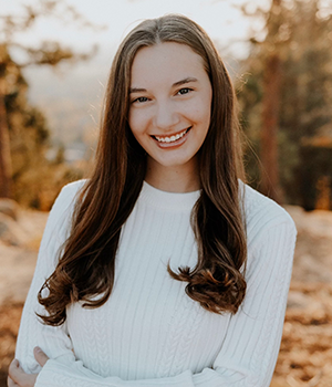 A girl with long dark hair and a white long sleeved shirt with her arms crossed