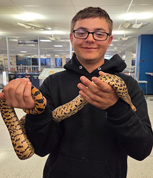A man with short brown hair and a black sweatshirt and glasses on holding a snake