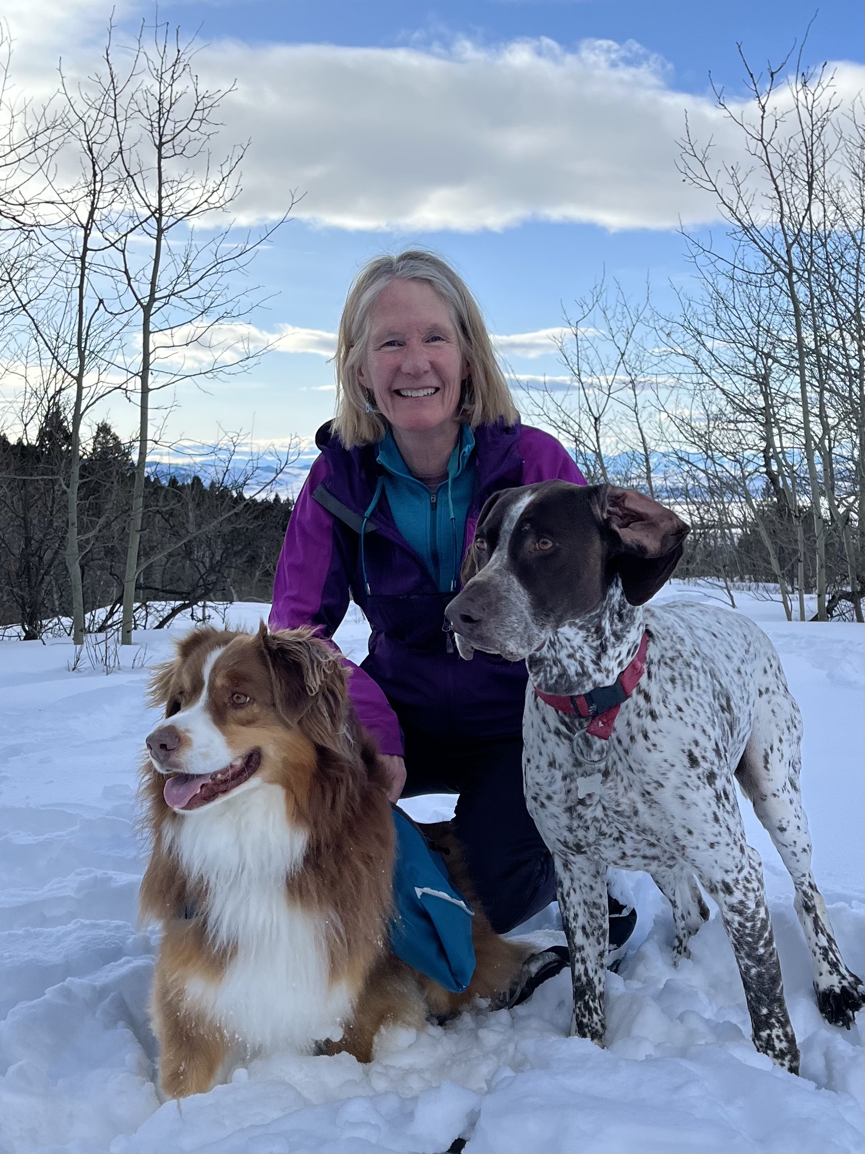 A woman kneeling down with two medium sized dogs smiling at the camera