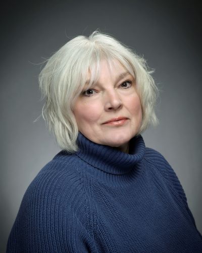 A woman with shoulder-length gray white-gray hair wearing a blue turtle neck