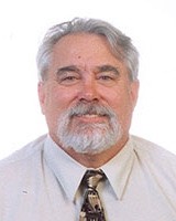 A man with short gray hair and a gray beard smiling to the camera