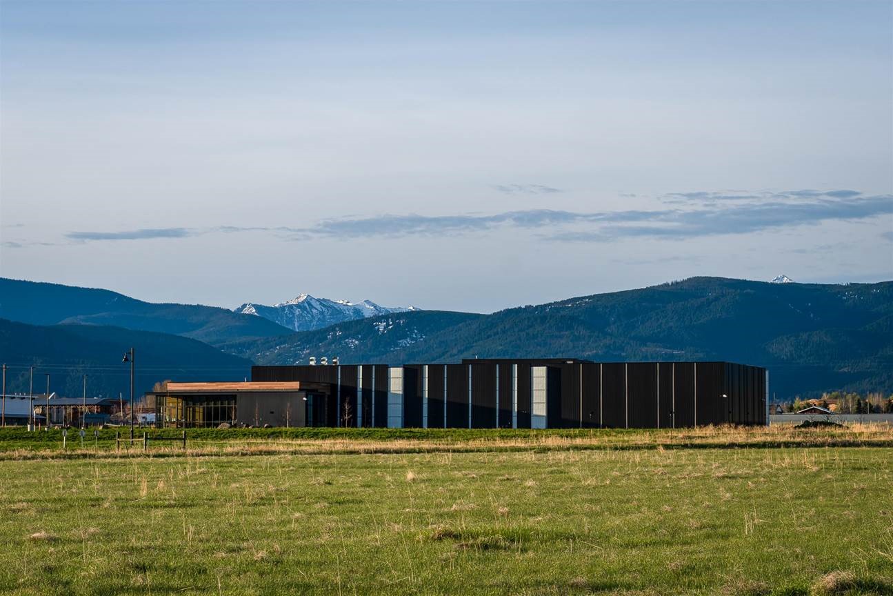 Large industrial building with mountains in the background, and spring-type grasses in the foreground. 