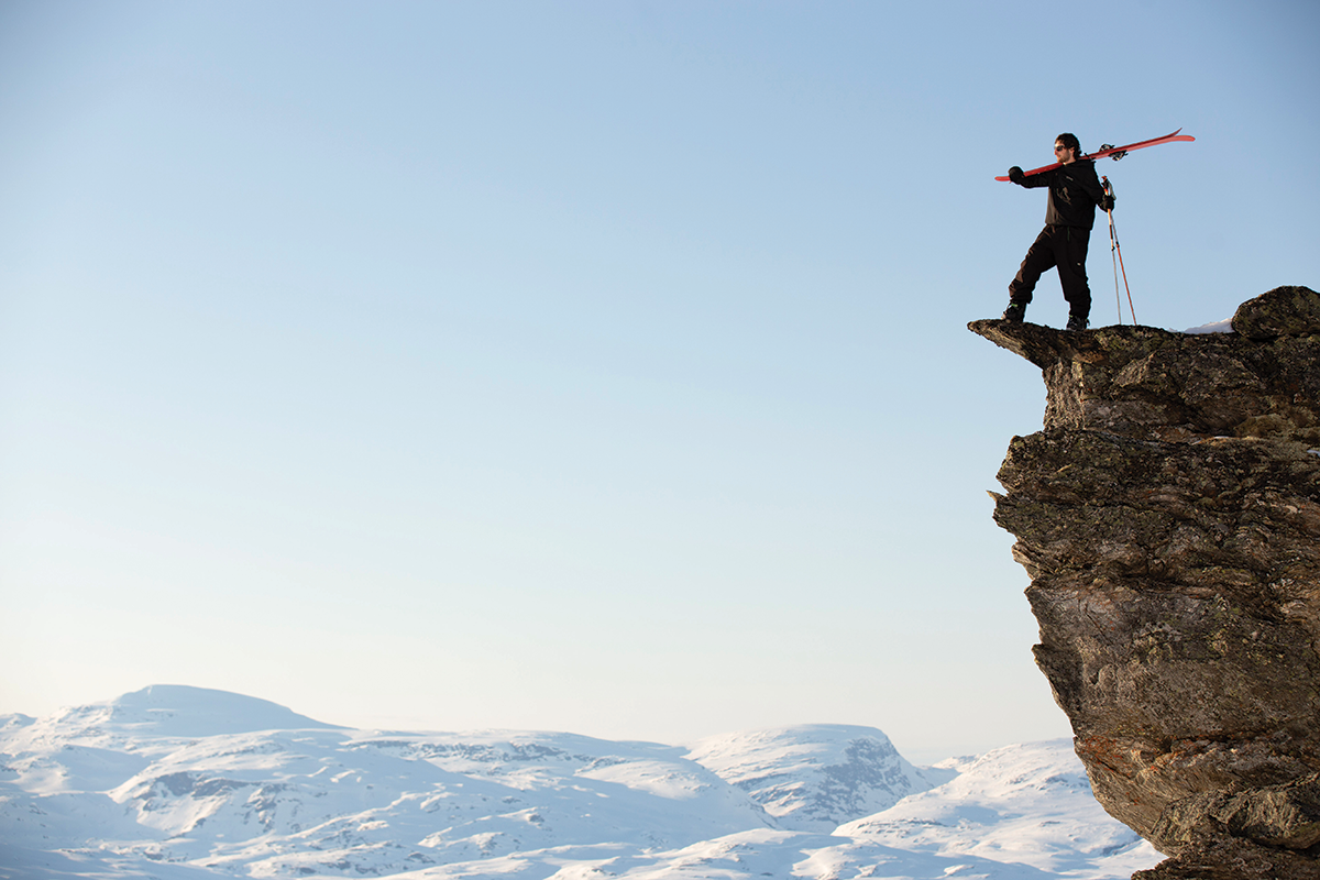 A person holding skis standing on a cliffside