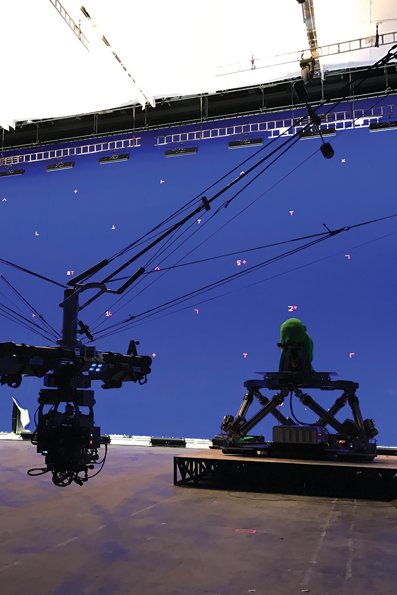 A studio camera pointing at a figure on a small platform with a purple backdrop