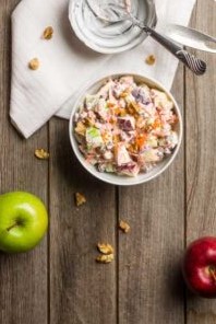 A table with a bowl of apple salad, a bowl of yogurt, a red apple, a green apple, and cereal.