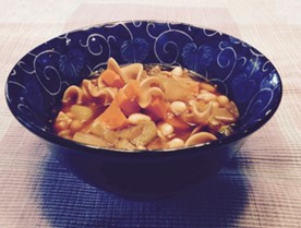 A bowl of soup that includes noodles, beans, and vegetables. 