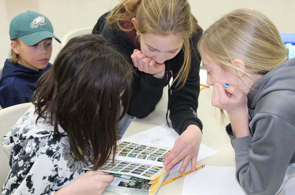 Group of three students hover over a book .