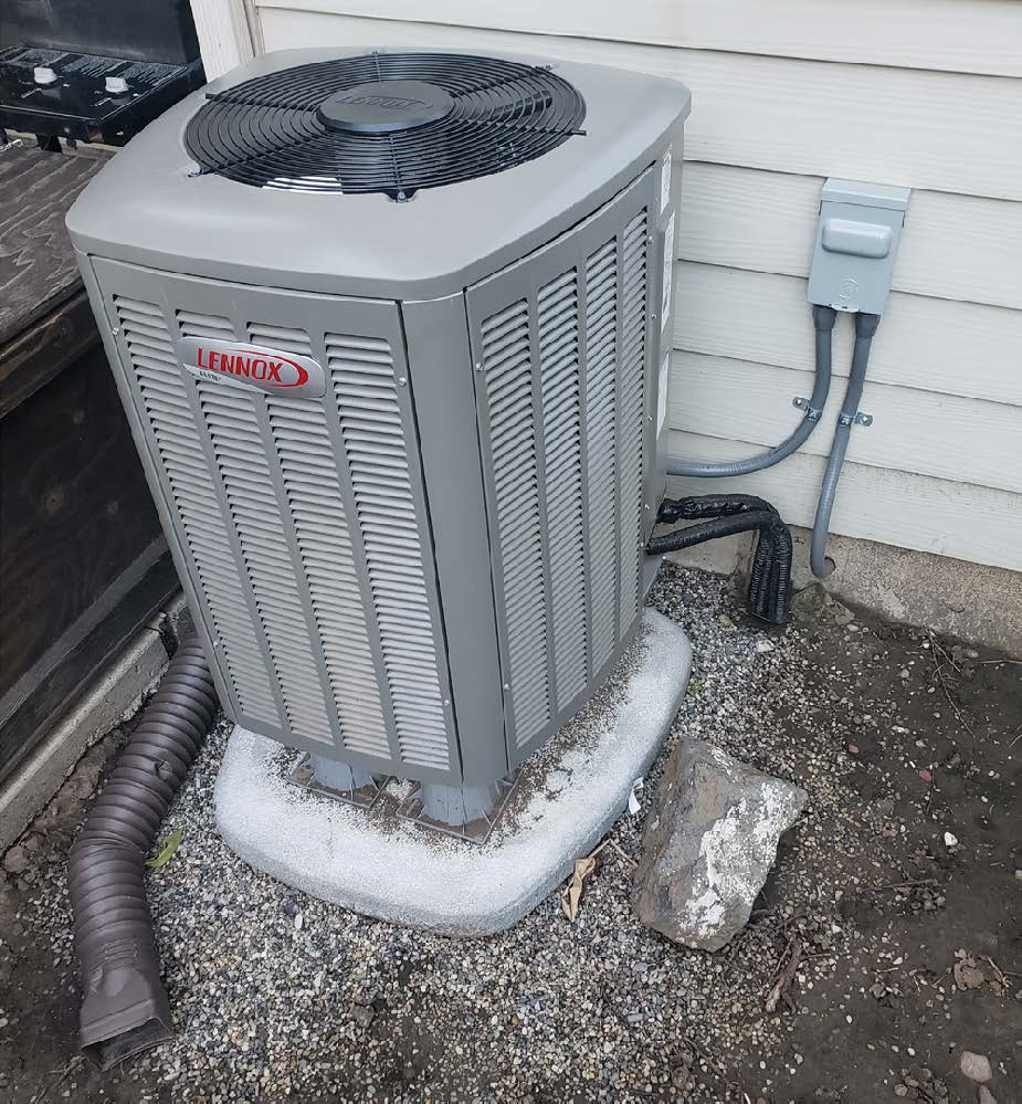 A large outdoor, grey heating pump that sits on the edge of the house, connected to the wall by cords.