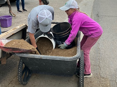 Beyond Time and Measure article feature Two kids load sand into buckets from a wheelbarrow.