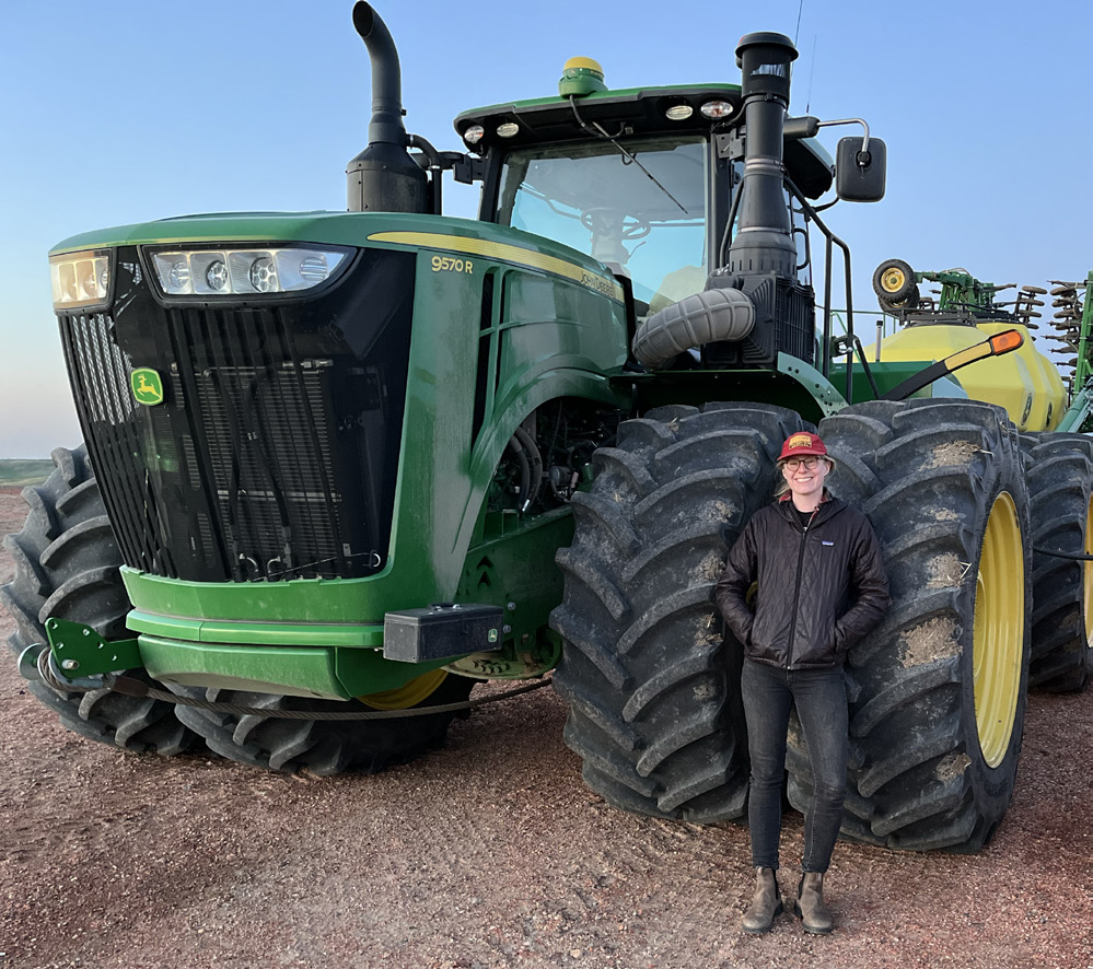 Megan Torgerson in front of a large, green John Deer tractor.