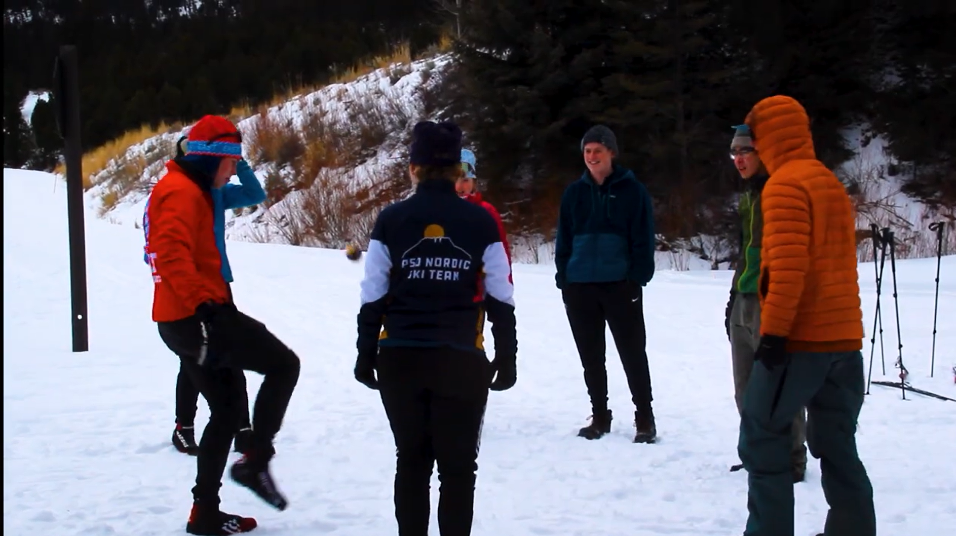 A group of students wearing jackets, hats, and boots, standing in a circle in snow