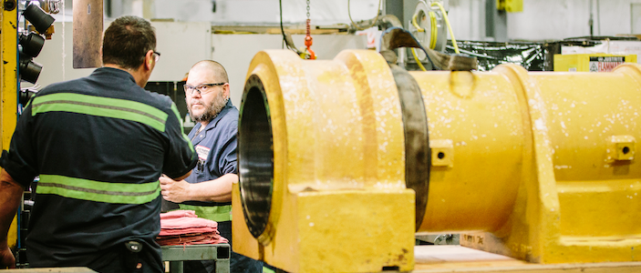 two mena in manufacturing facility with yellow machinery