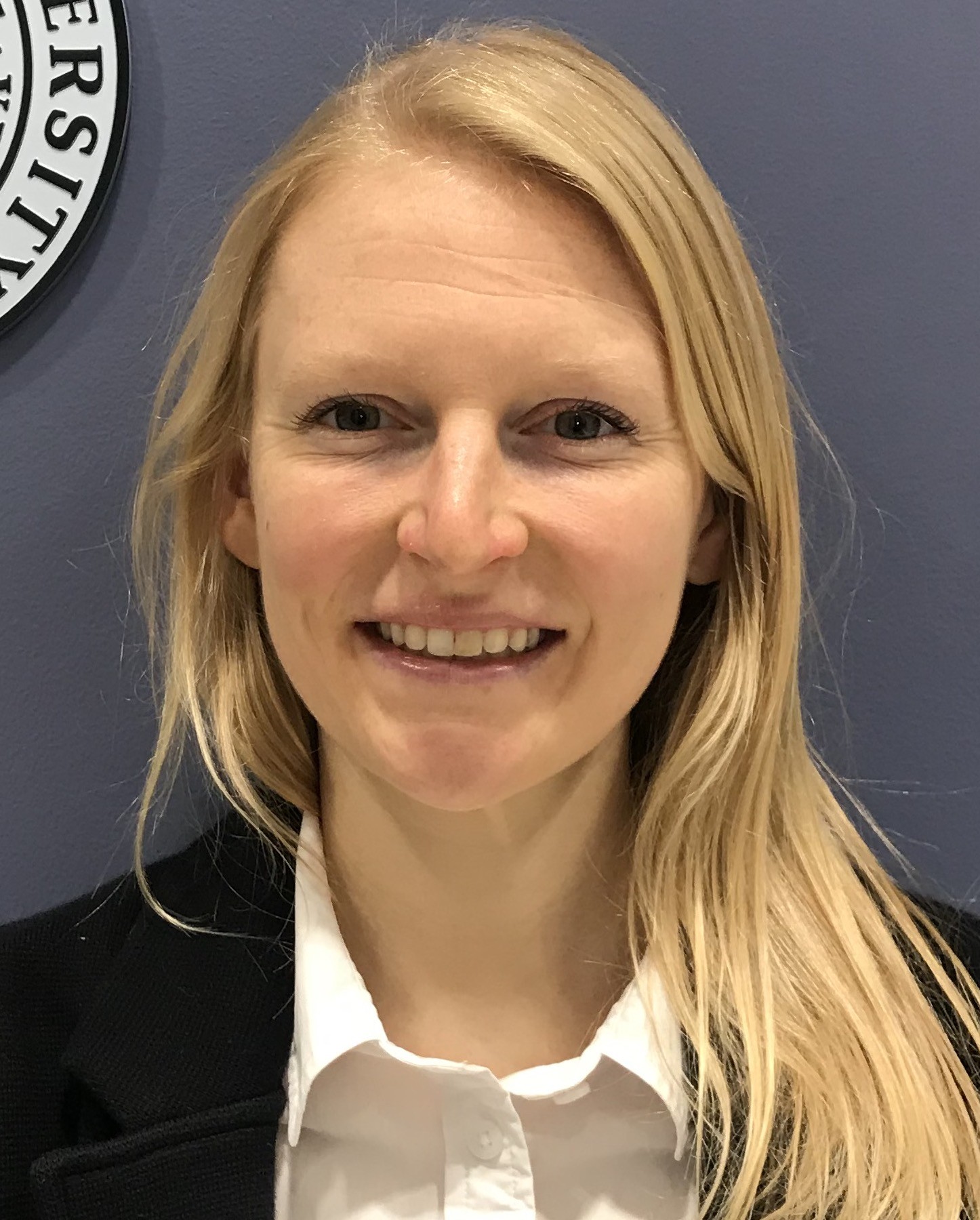 Professional headshot of a blonde long haired person wearing a white button up shirt
