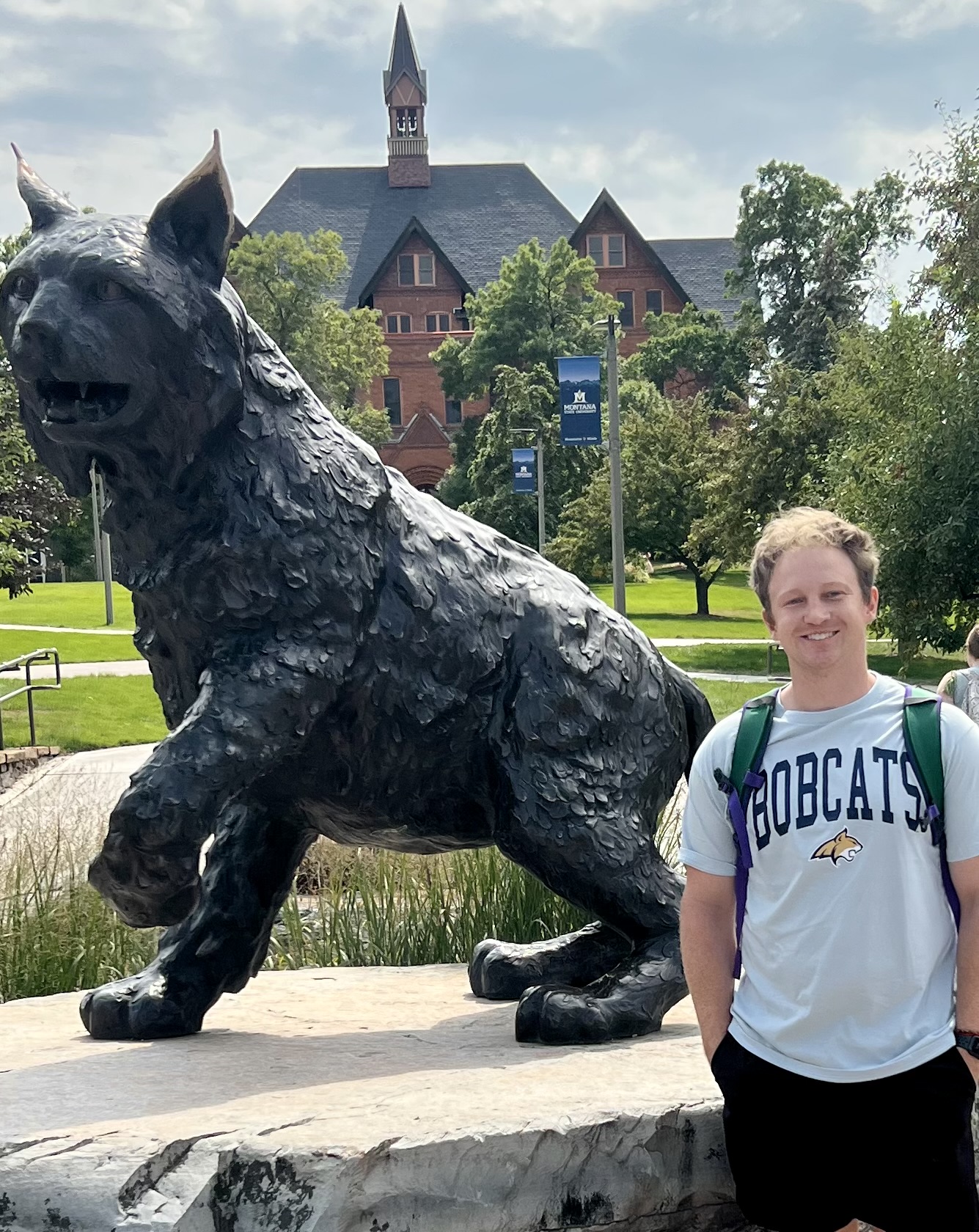 A person wearing a gray BOBCATS crewneck standing next to a bobcat statue