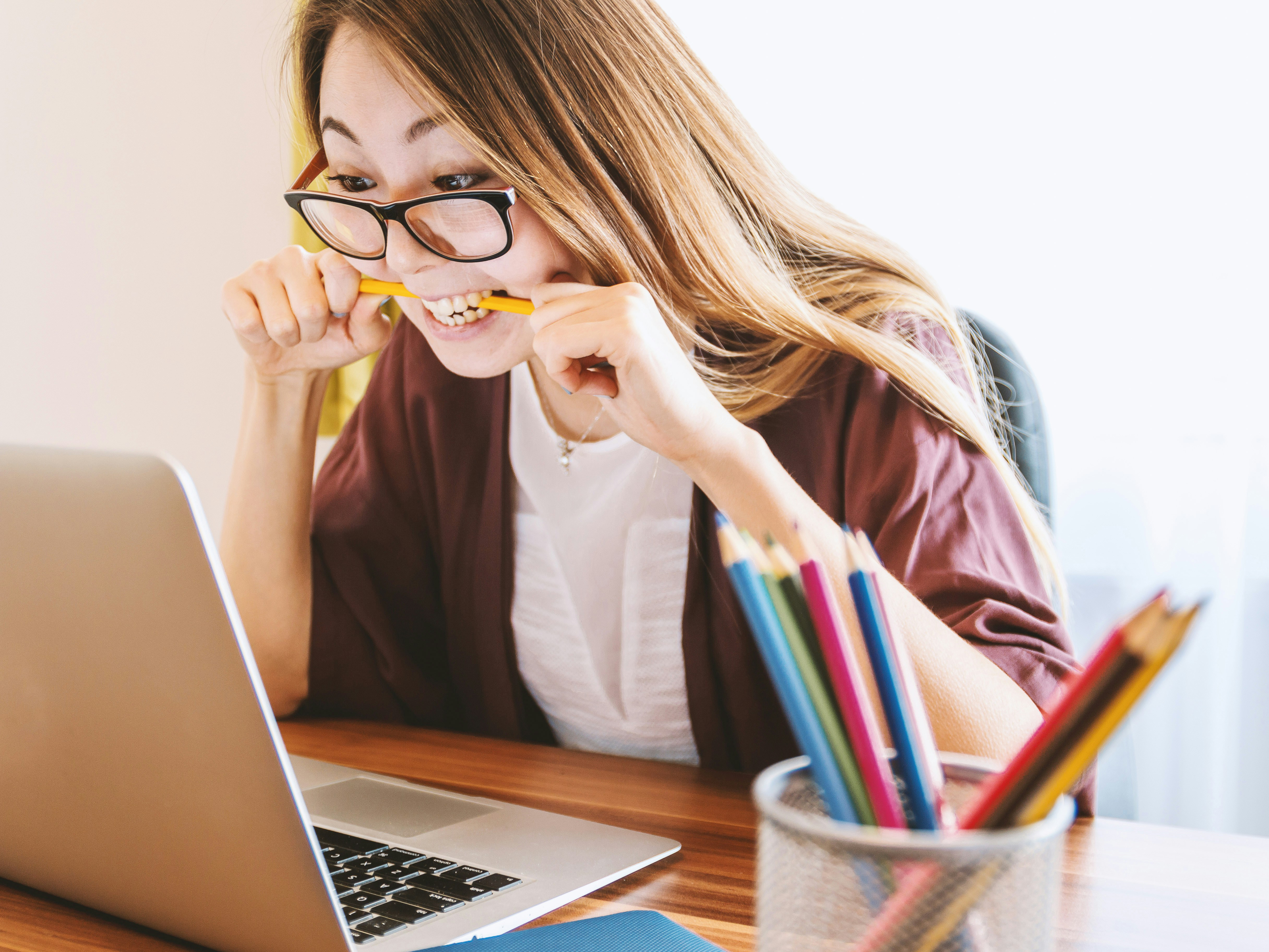 Stock image of a woman biting her pencil while looking at her laptop screen