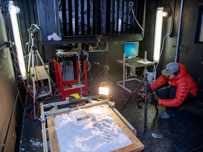 MSU student in orange puffy coat working on snow experiment in freezer room