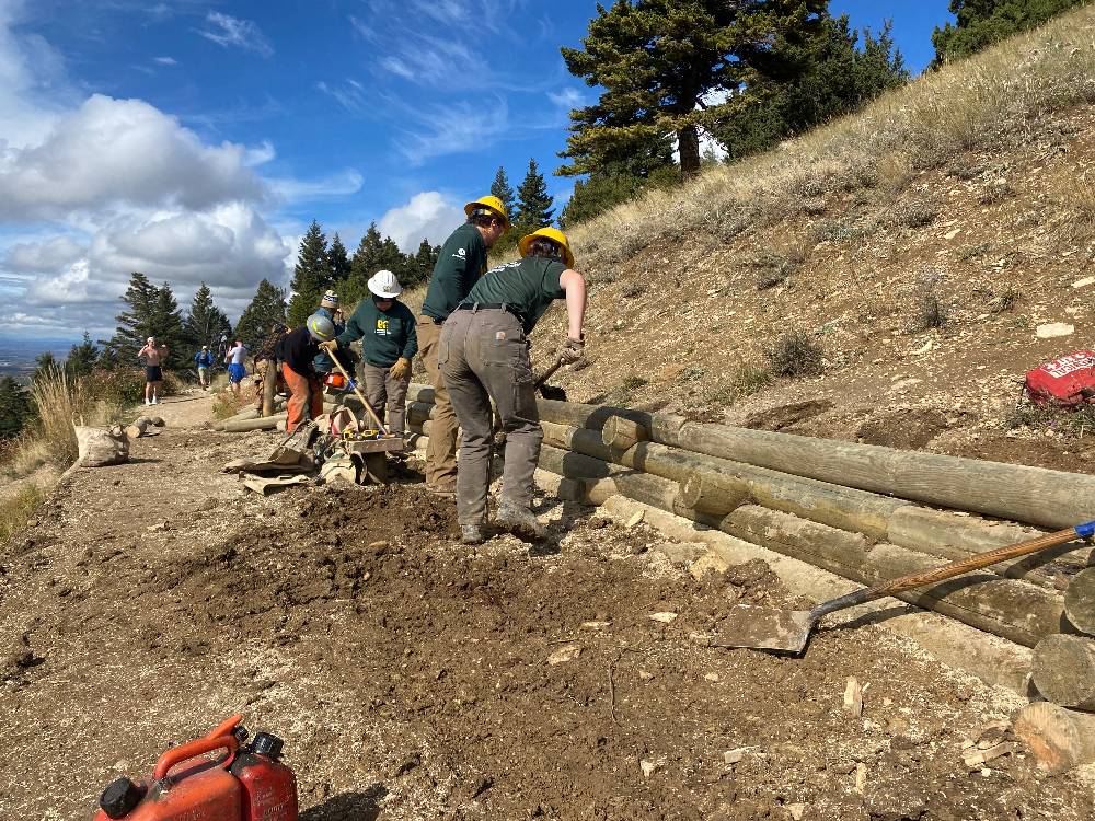 A group of people wearing green shirts and hard hats work on The M trail's outlook platform.