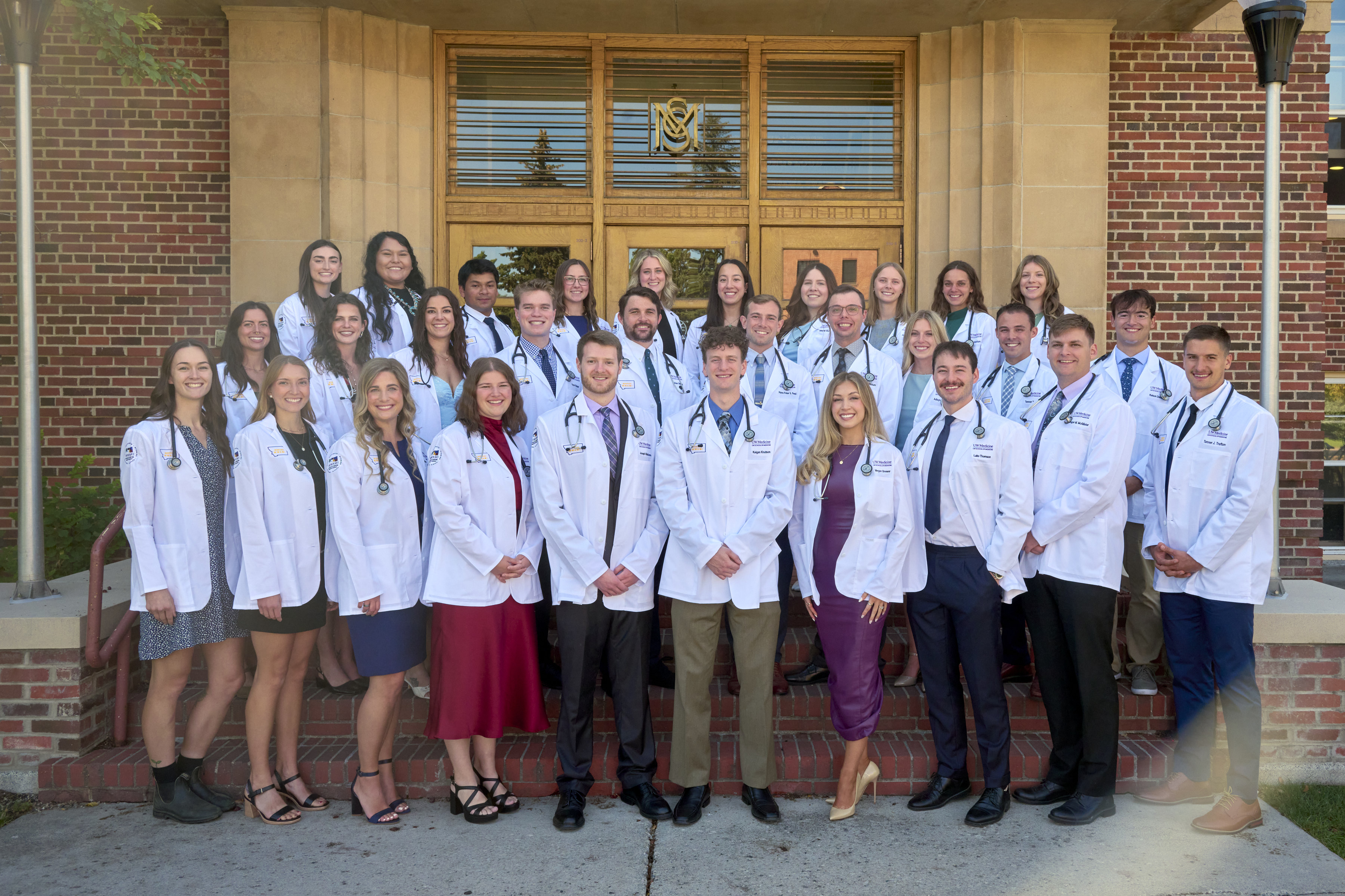 E25 White Coat A group of 30 male and female medical students posing in their white coats in front of a brick building